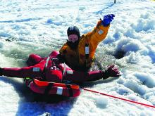 Viktor Sundleaf (in yellow) signals to his fellow firefighters that the victim, Jason Bame (in red) is secure and ready to be pulled out of the hole in the ice. Photo courtesy of Kevin Carl