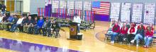 Panther senior Noah Graham speaks at the podium during DV's Veterans Day Program. To the left are seated local veterans and to the right, in seats, are DV student council members.