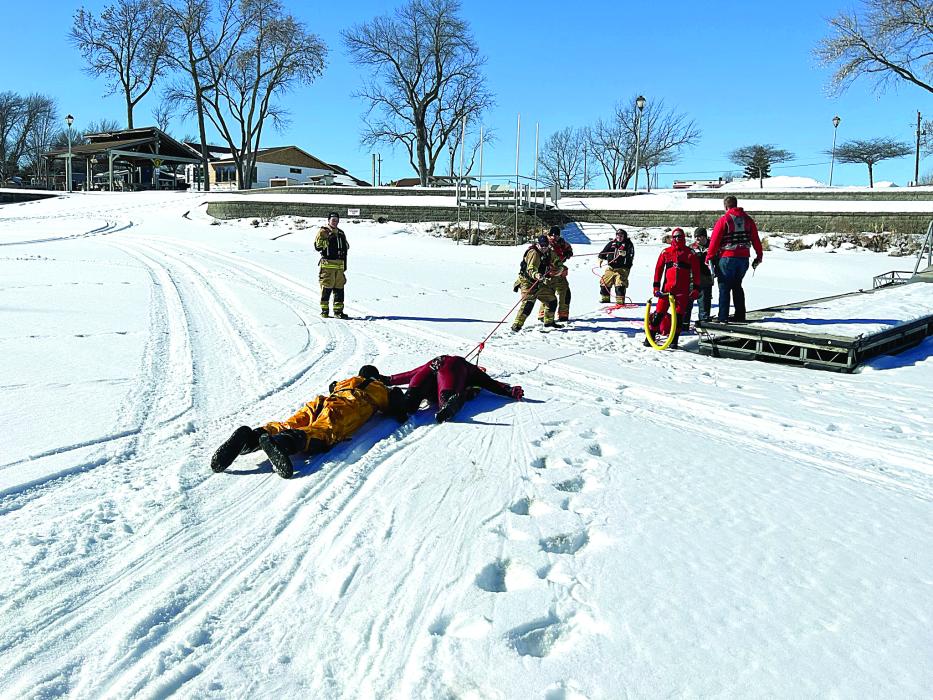 Viktor Sundleaf (in yellow) and victim, Jason Bame (in red) are pulled carefully across the ice toward the shoreline. Pulling the two to safety are Levi Saunders, Carter Matousek and Kale Kriese. Watching on the left is Evan Carlson. Watching from the right are Adam Spates, Brett McCabe and Nick Buckley. Photo courtesy of Kevin Carl