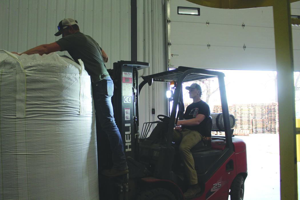 Evan Fornia waits as a bag is tied by Mark Pals before transferring it to another location inside the warehouse. Photo by Beth Hutcheson • times1reporter@gmail.com