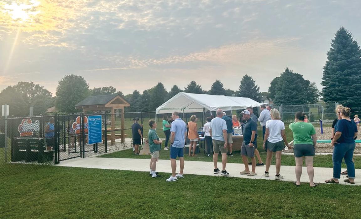 Area residents line up for treats under the tent during the grand opening and ice cream social for the new North Sioux City dog park on Wednesday, Aug. 12. (Inset) Custom-painted decorative fire hydrants, including a Dalmatian and a Dakota Valley Panthers theme, add local flair inside the new Barks &amp; Rec Dog Park.