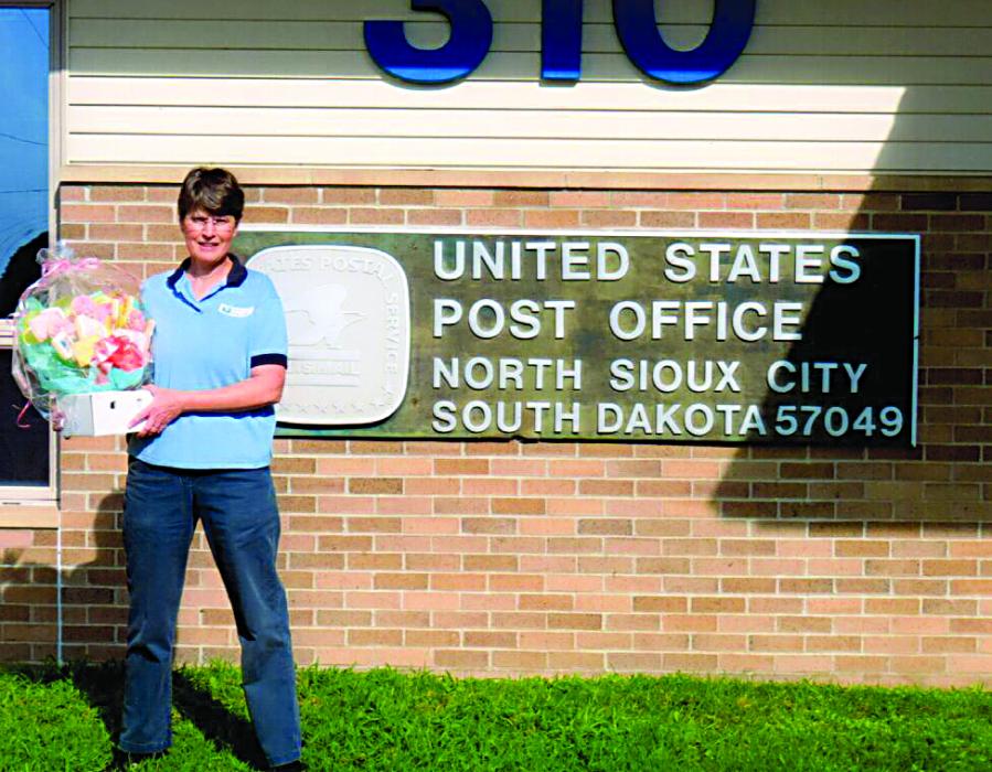 Susanne Piplani stands outside the North Sioux City Post Office with a gift basket during her final week on the job. Piplani is retiring after more than 27 years as a USPS clerk and trainer. Submitted photo