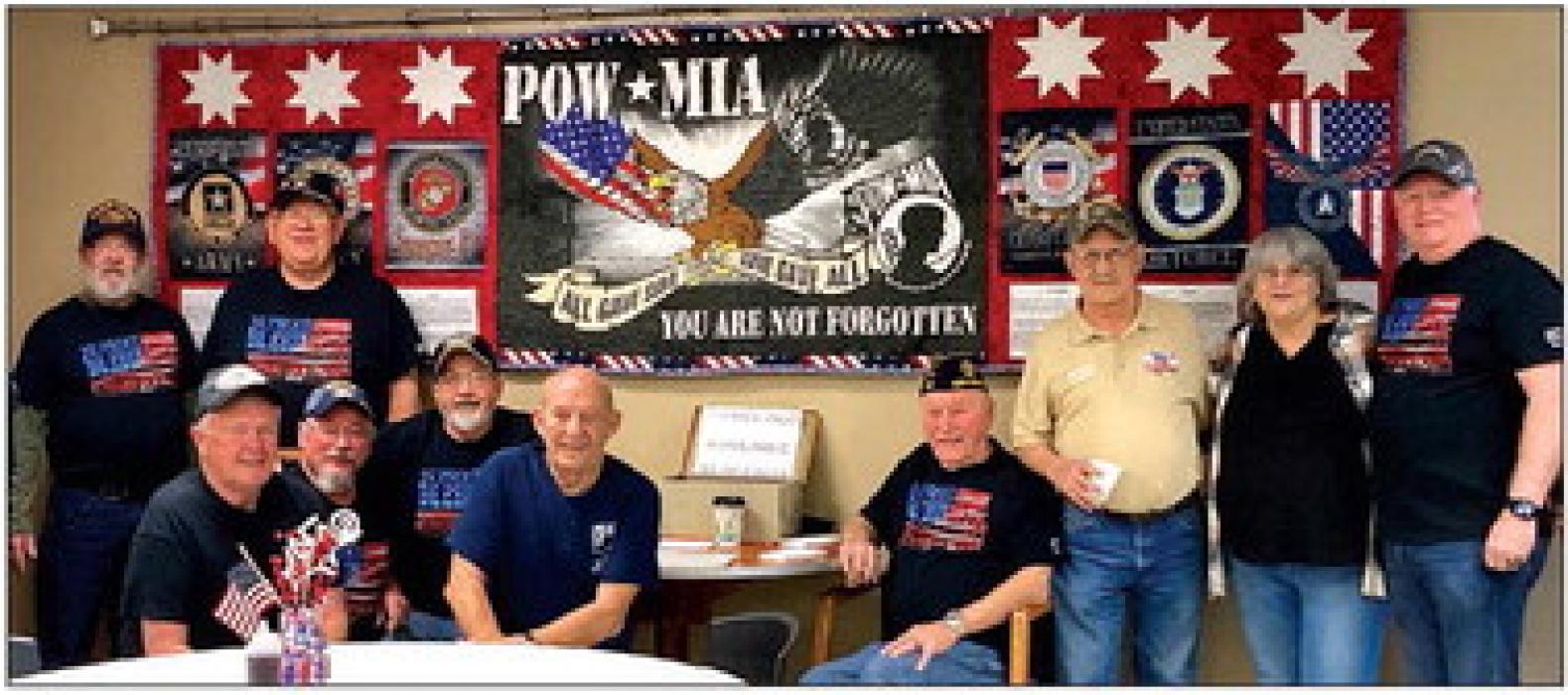 Members of American Legion Post 319 of North Sioux City are pictured with Jerri Bailey (second from right) and the quilted banner (in the background) that she made honoring all the branches of service. Photo courtesy of Lisa Schenzel